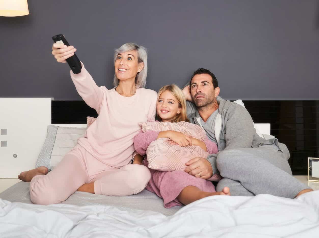 family in bed in pajamas watching TV